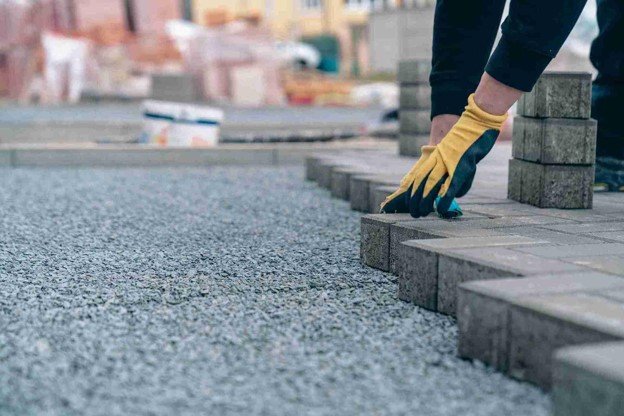 Worker placing concrete pavers on gravel base for professional driveway installation