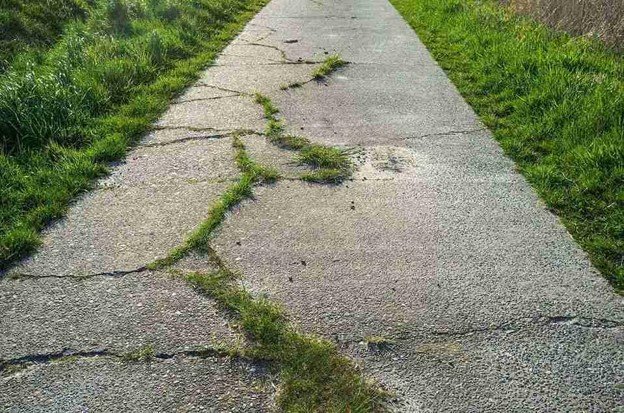 Cracked and damaged concrete driveway with visible wear and weeds growing through surface in North Ridgeville, OH